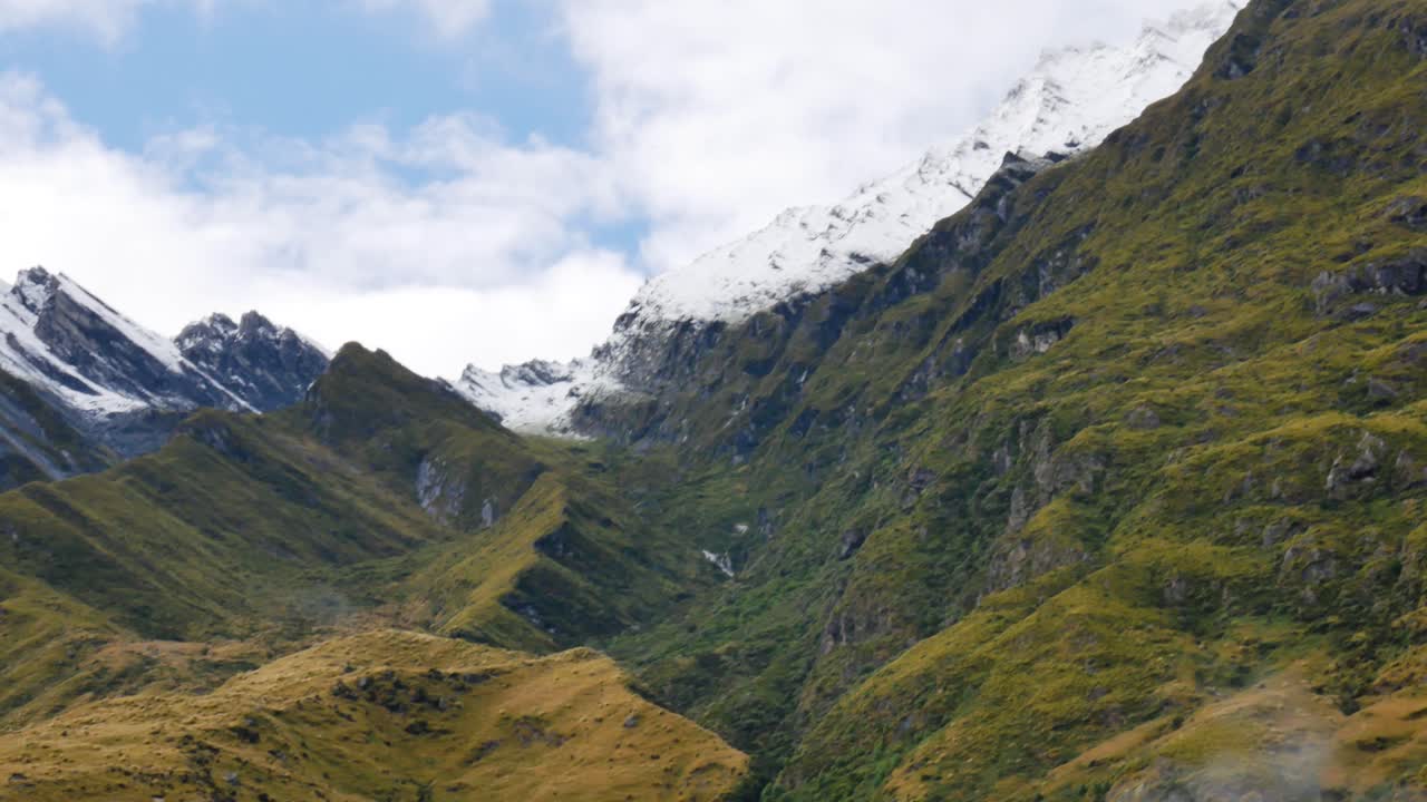snow capped peaks yield to green covered slopes in mountain valley