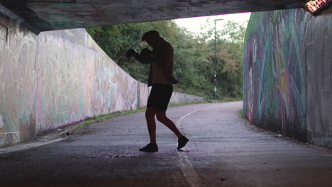 wide shot of a young athletic man boxing in an underpass, silhouetted by the light behind him