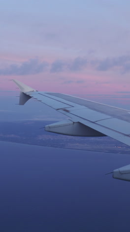 view from a plane window of the sky at sunrise with the wing of the plane in shot in vertical