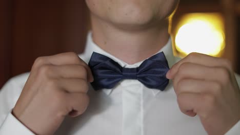 man putting on a blue bow tie before wedding