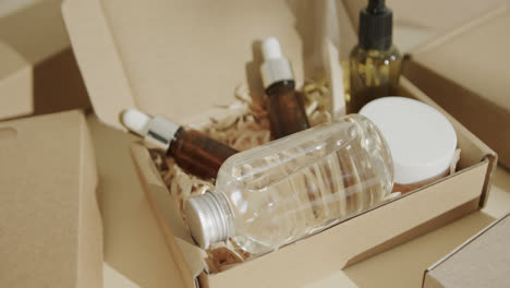 Close-up-of-cardboard-boxes-with-glass-bottles,-cream-tub-and-toothbrush-on-beige-background