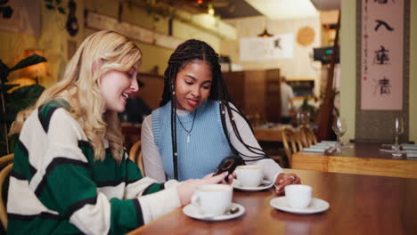 two women looking at a phone in a cafe