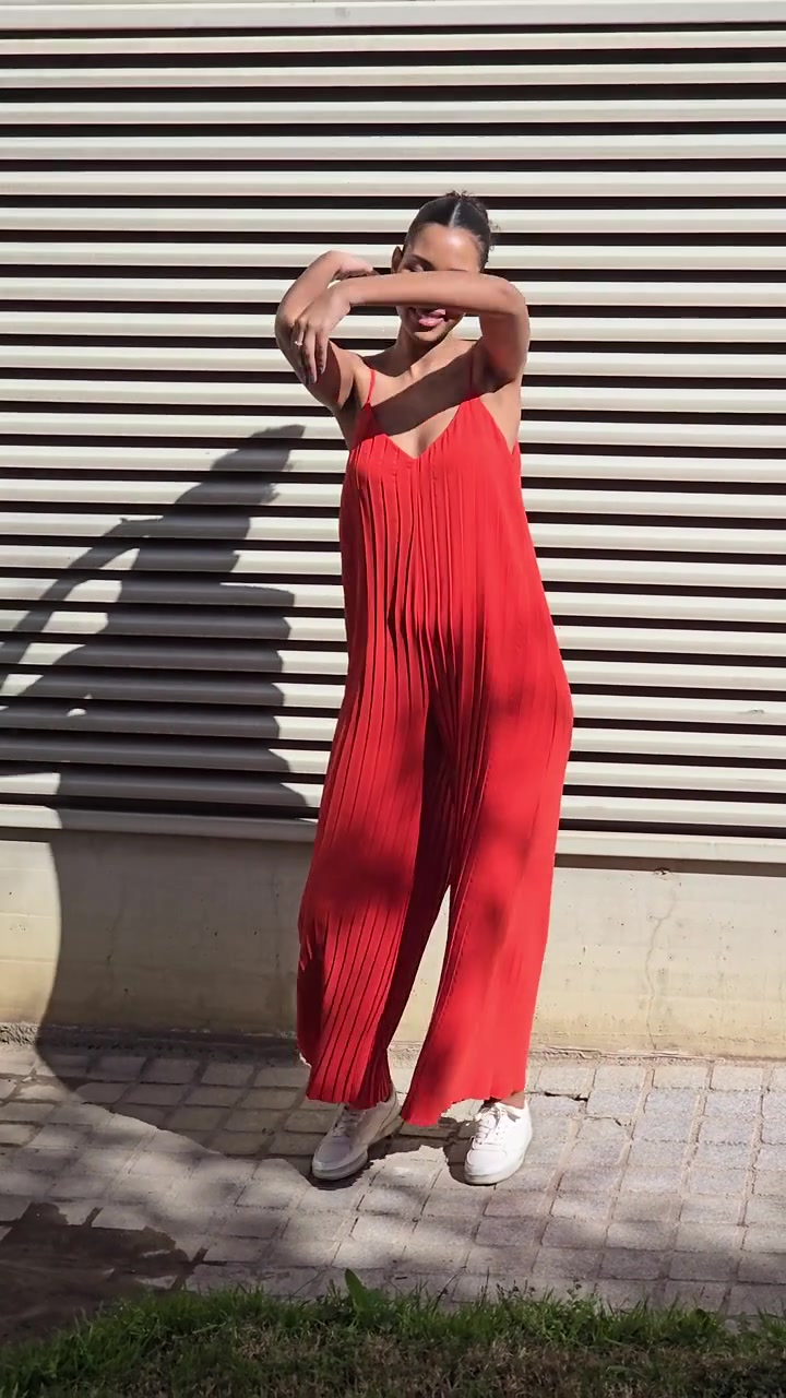 Una donna alla moda che indossa un'audace tuta rossa posa contro una parete strutturata