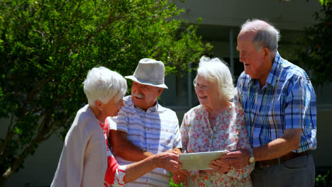 Grupo-De-Parejas-Mayores-Caucásicas-Discutiendo-Sobre-Una-Tableta-Digital-En-El-Jardín-De-Una-Residencia-De-Ancianos-4k