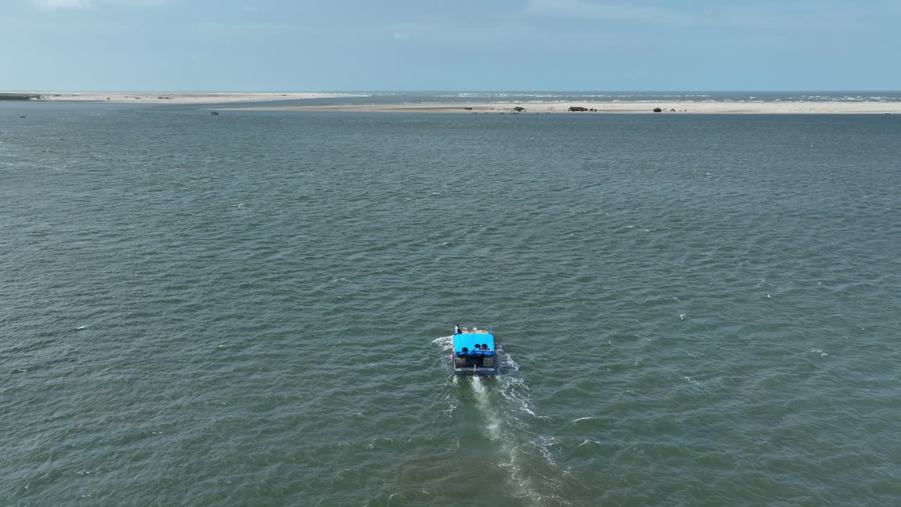 Aerial: blue boat on Atlantic Ocean in Lencois Maranhenses National Park during the day in Maranhao state, northeastern Brazil, pull out drone shot