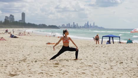 woman practicing yoga and doing extended side angle - surfers paradise from burleigh heads beach in qld, australia