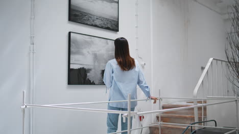 girl looking gallery paintings rear view. young designer drinking water resting