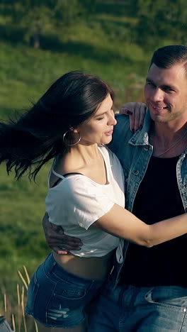 young brunette woman in white t-shirt jumps in handsome muscular man arms against green meadow slow motion