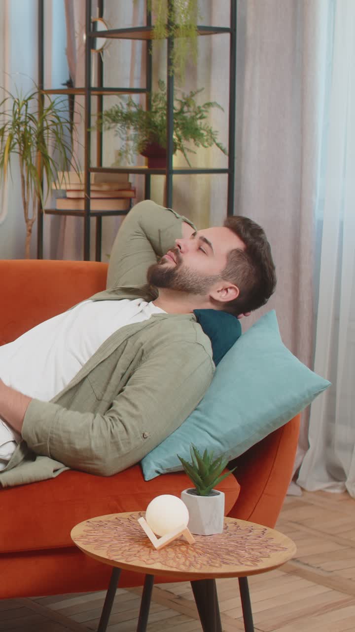 Tired caucasian handsome young man enjoy relaxing lying on sofa in living room at home apartment