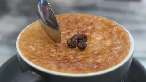 with the help of a spoon, breaks the crystalized hard brittle layer of caramel of a cup of brulee coffee and decorated with coffee beans