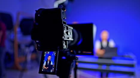 brunette girl on the camera display. blog recording. man walks at blurred backdrop behind the stages.