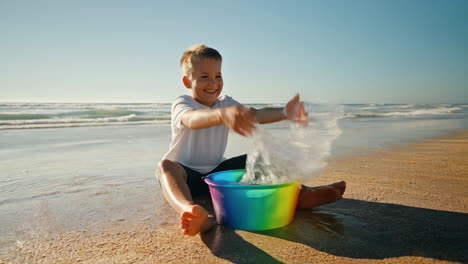 happy boy playing with a colorful bucket on a sunny beach