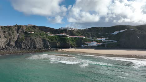 Aerial-shot-flying-over-turquoise-water-towards-houses-on-cliffs-under-a-blue-sky