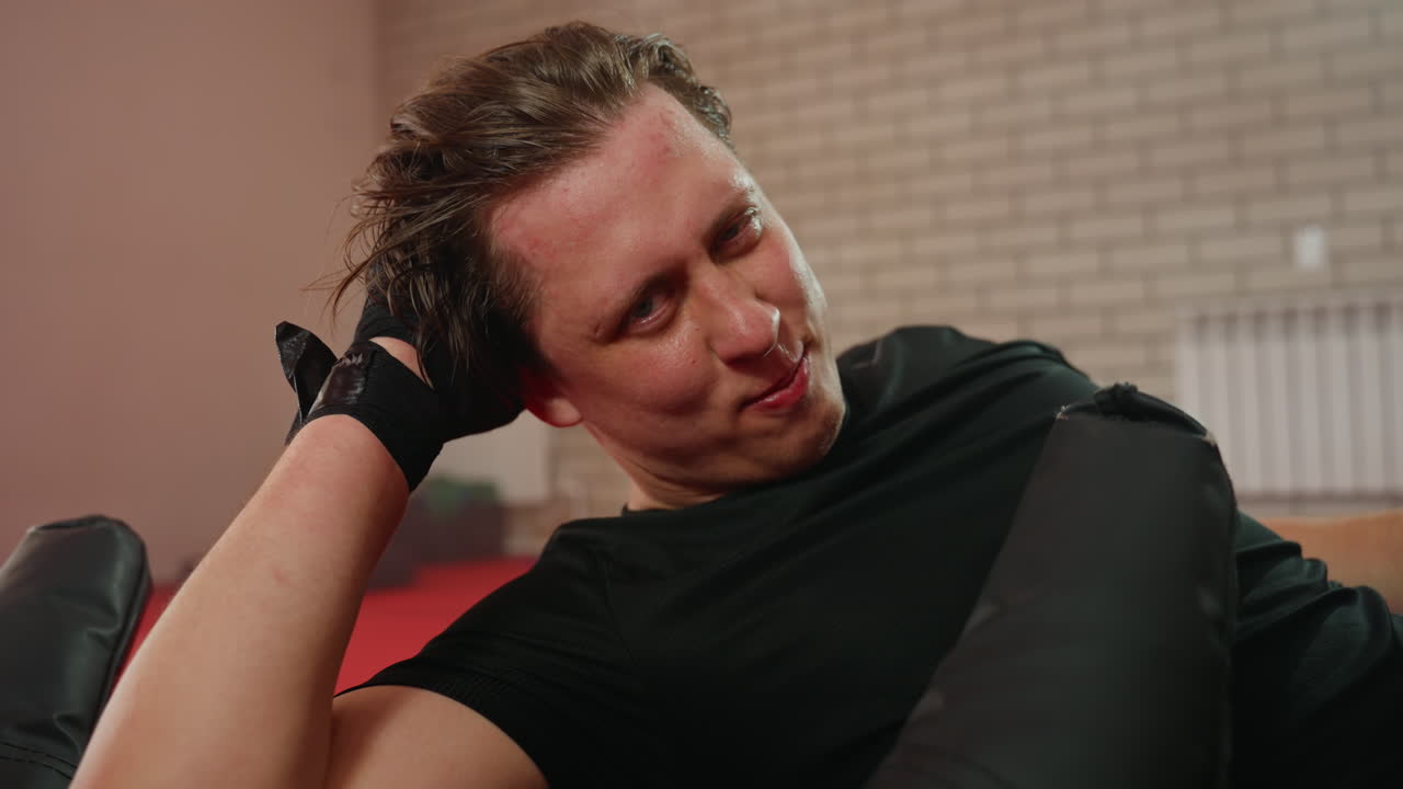 Boxer lying on training mat after workout with sweat on face and gloves on hands, exhausted but determined, demonstrating effort, strength, and perseverance during intense combat sports fitness session