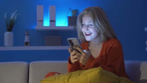 Mujer-Joven-Riendo-Usando-El-Teléfono-En-Casa-Por-La-Noche.