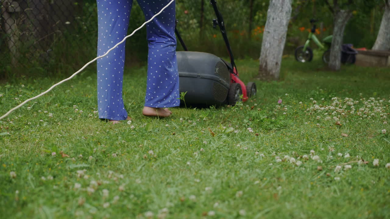 human is controlling the work of lawn mower near the path in the yard in the summer. The lawn mower consistently is mowing grass