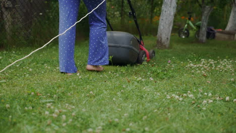 human is controlling the work of lawn mower near the path in the yard in the summer. the lawn mower consistently is mowing grass