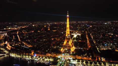 Eiffel-tower-automated-light-beams-sparkling,-Paris-cityscape-and-skylines-at-night,-Aerial-pullback-shot