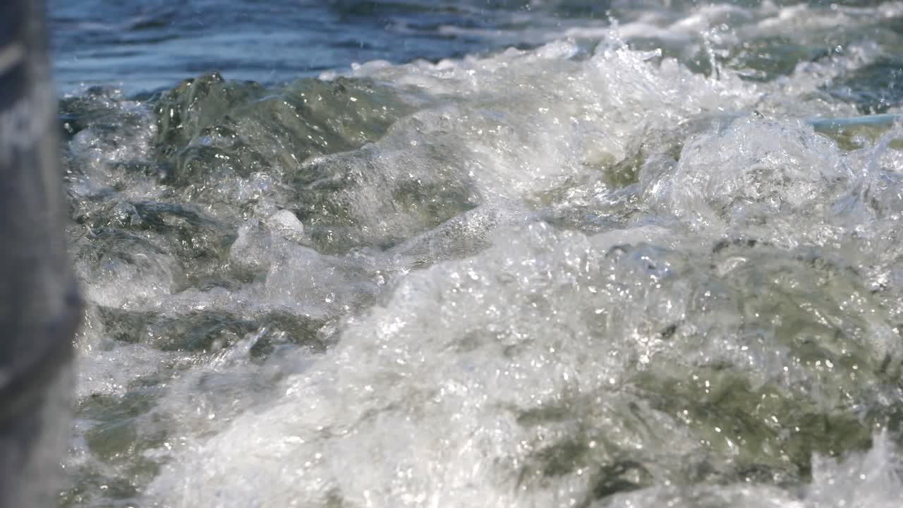 Espuma da esteira azul do oceano movendo-se atrás do motor do barco em câmera lenta, com profundidade de campo rasa