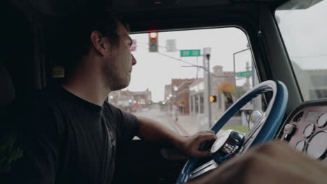 Young-truck-driver-shifting-gears-driving-through-city-in-cockpit-view