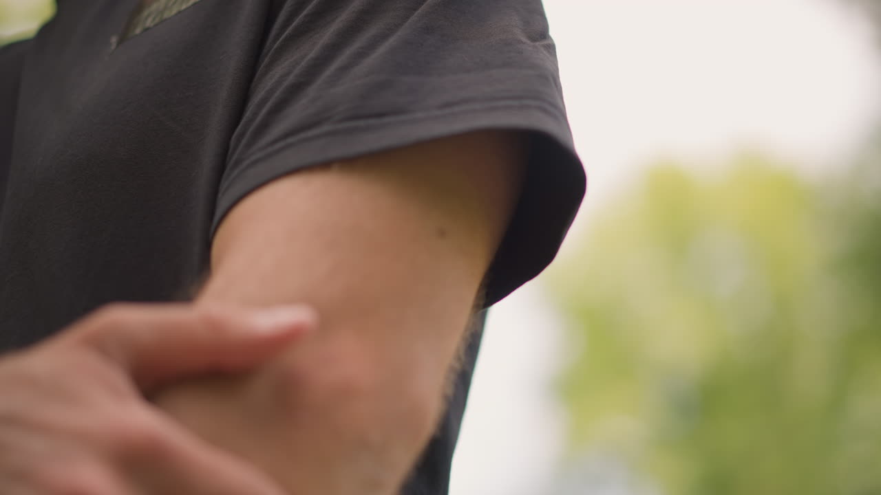 Casual Attire With Relief From Itching Observed, Person Checking Upper Arm Itch During Relaxed Park Afternoon Moment, Casual Scene Of Scratching And Relief On Upper Arm In Sunny Park Atmosphere