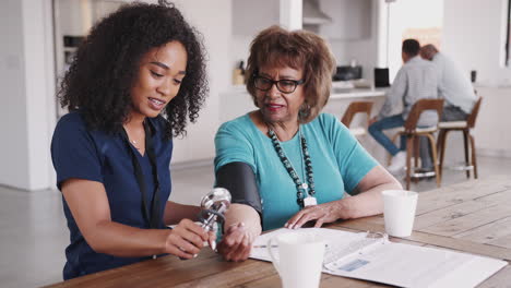 female healthcare worker checking the blood pressure of a senior woman during a home visit