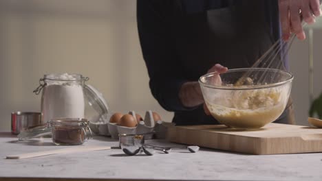 primer plano del hombre en la cocina de casa batiendo los ingredientes al tazón para hornear pasteles