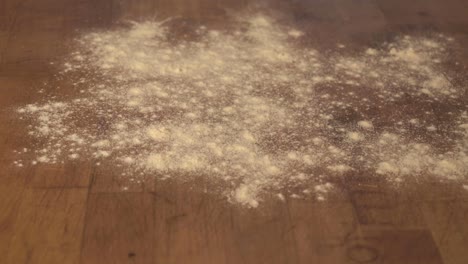 Preparing-the-wooden-table---cutting-board-for-cookie-dough-by-pouring-and-distributing-flour-on-it