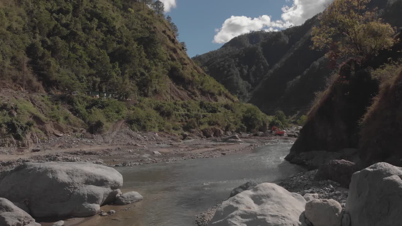 río rocoso que serpentea a través de las montañas en el valle del cañón agua que fluye acercándose rocas grises árboles verdes cielo azul y nubes antena lenta avance suave proximidad al pájaro que vuela a través