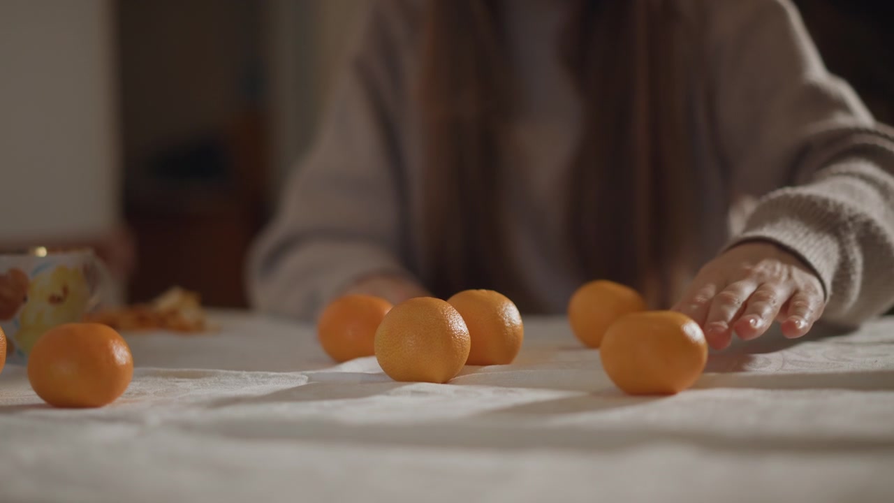 Tangerinas sobre a mesa, mãos de mulher caucasiana movendo a fruta, foco raso em close-up na fruta cítrica rolando, toque tátil em superfície de linho, bokeh cinematográfico, textura macro, estudo artístico lúdico e cotidiano de mesa.
