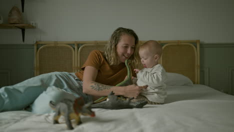 mother and baby playing with dinosaurs on bed