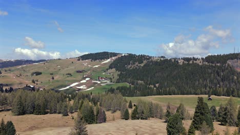 aerial view of rolling hills with patches of snow and dense forests in alpe di siusi, dolomites, italy, under a clear blue sky