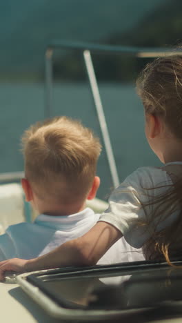 smiling little children lean out of cabin exit riding motorboat in scenic sea. cheerful brother and sister sail modern yacht in ocean on summer holiday