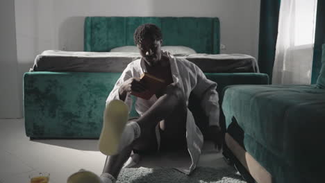 man in bathrobe sitting on bed, brushing hair with hairbrush in cozy bedroom. velvet green bed, relaxed mood, natural light streaming through window, peaceful morning routine