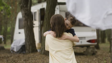 Loving-mother-crouching-while-her-happy-son-is-running-into-her-arms-at-the-camping-in-the-forest