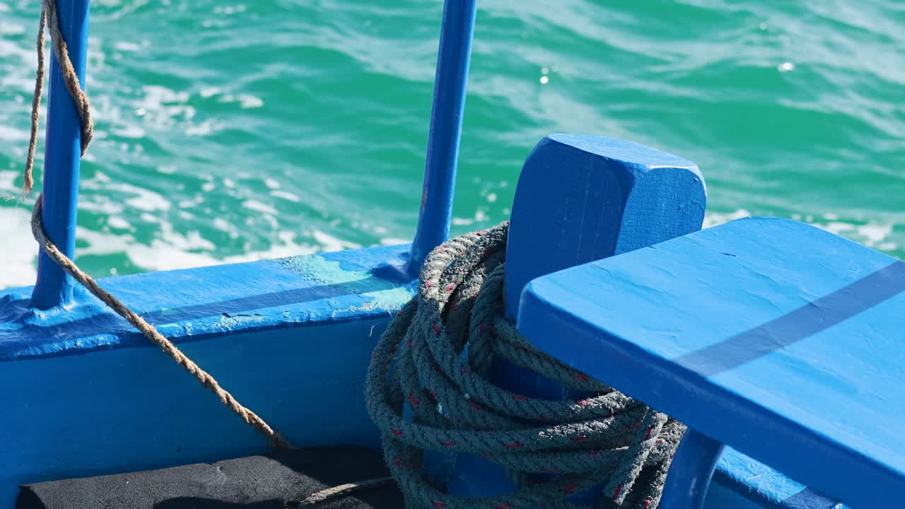 A blue fishing boat with coiled rope navigates vibrant turquoise waters under bright sunlight in Phuket, Thailand