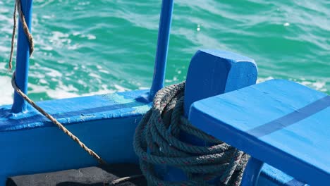 a blue fishing boat with coiled rope navigates vibrant turquoise waters under bright sunlight in phuket, thailand