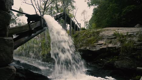 el agua pasa por el antiguo molino de río de madera y cae de la construcción