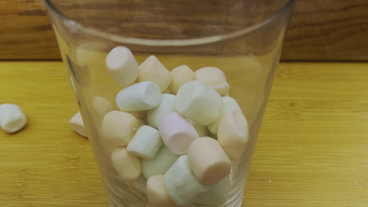 Farverige skumfiduser fylder et klart glas til sød snack eller dessertforberedelse, der viser bløde konfekture-pastelfarver og legende madpræsentation.
