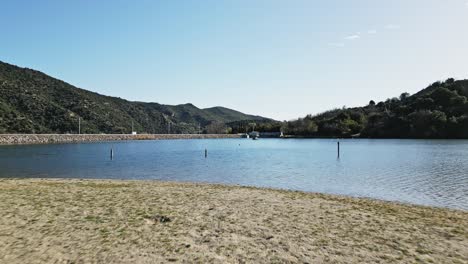 Ein-Hund-Holt-Den-Ball-In-Der-Natürlichen-Landschaft-Des-Lac-Vinça-Sees-In-Frankreich-Im-Warmen-Sommer,-Luftdrohne-Fliegt-Tief-Entlang-Der-Französischen-Pyrenäen