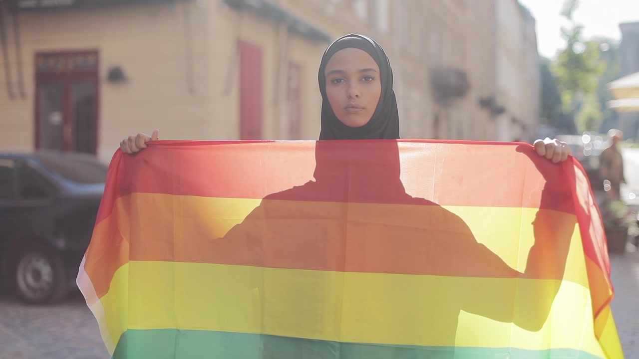 Young Woman Wearing Hijab Holding a Rainbow Pride Flag on City Street