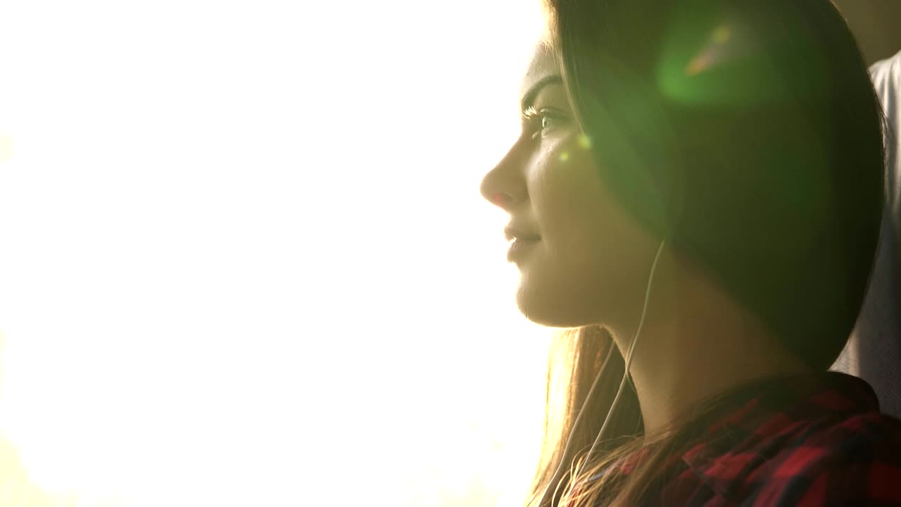 vista lateral de una hermosa chica caucásica yendo a algún lugar en tren. escuchar música en auriculares. mujer pensativa. sonriente. el sol brilla