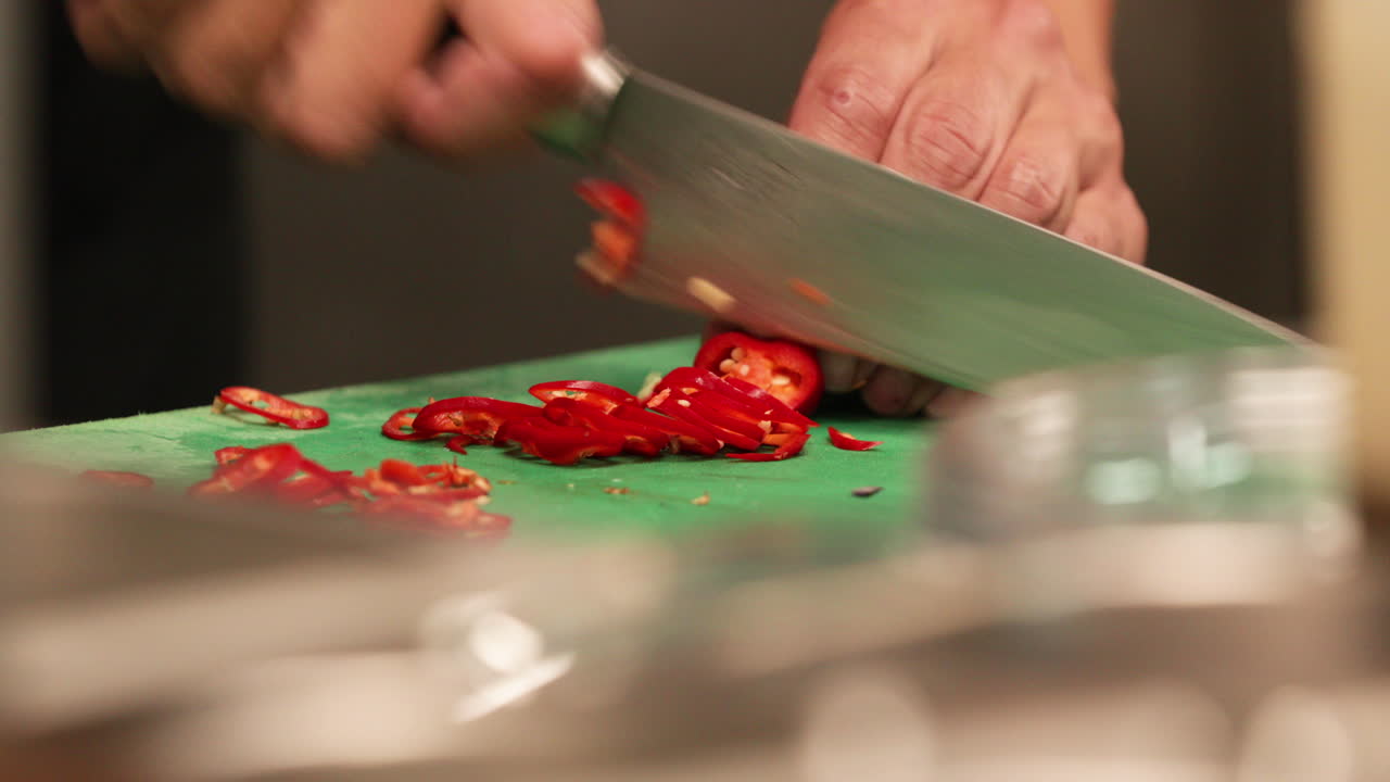 chef cortando chiles rojos en una tabla de cortar usando un cuchillo en la cocina de un restaurante