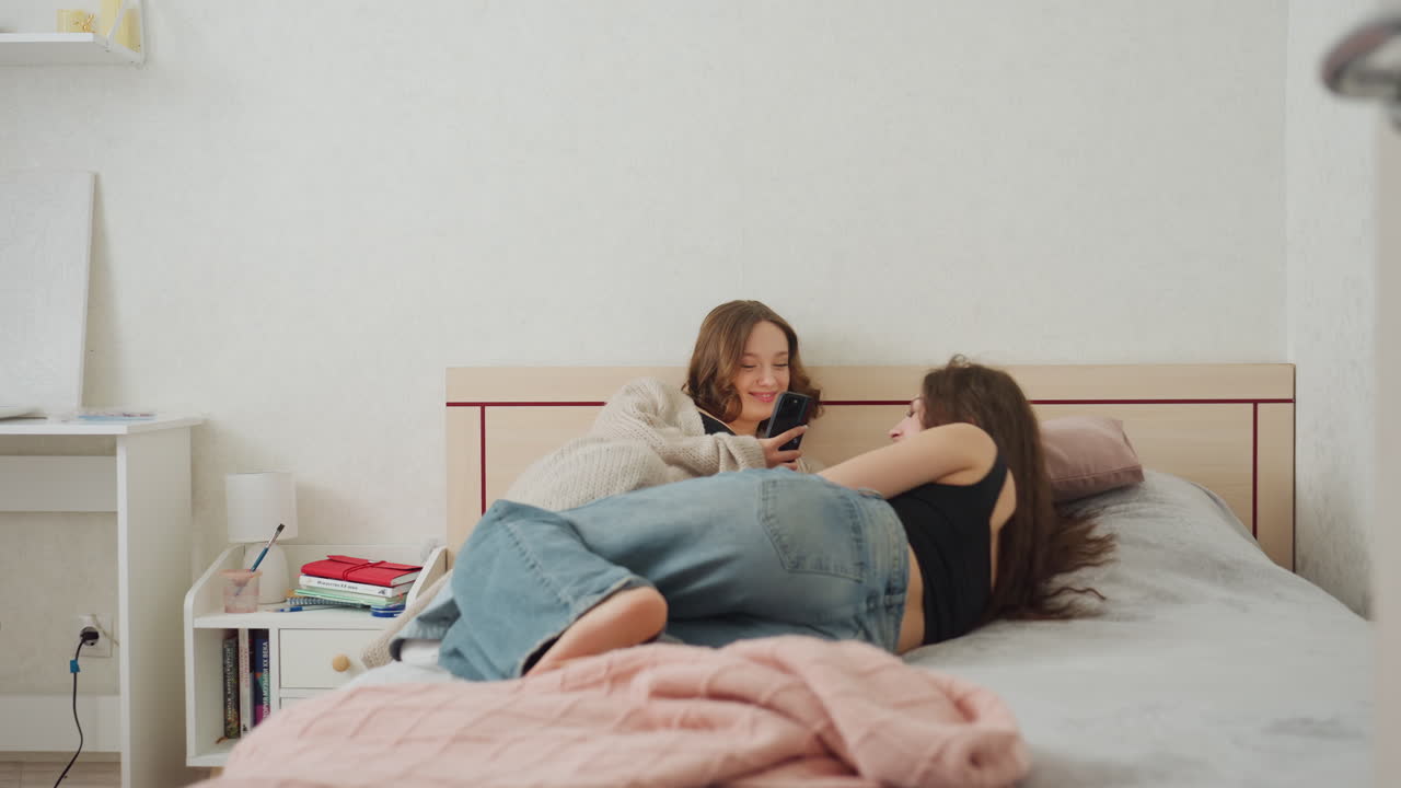 Caucasian Student Enters Shared Dorm Bedroom Carrying Books And Denim Skirt, Doorframe Perspective Shows One Roommate On Bed With Notebook And Blanket, Playful Chat And Study Vibe, Lamp And Desk