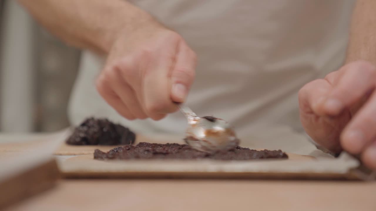 Person Spreading Plum Jam On Galette Using Spoon