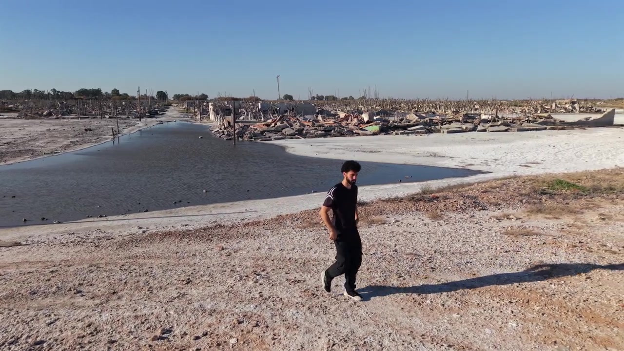 Vista aérea de um jovem caminhando sobre o solo coberto de sal e ruas inundadas da cidade fantasma abandonada de Villa Epecuén, Argentina