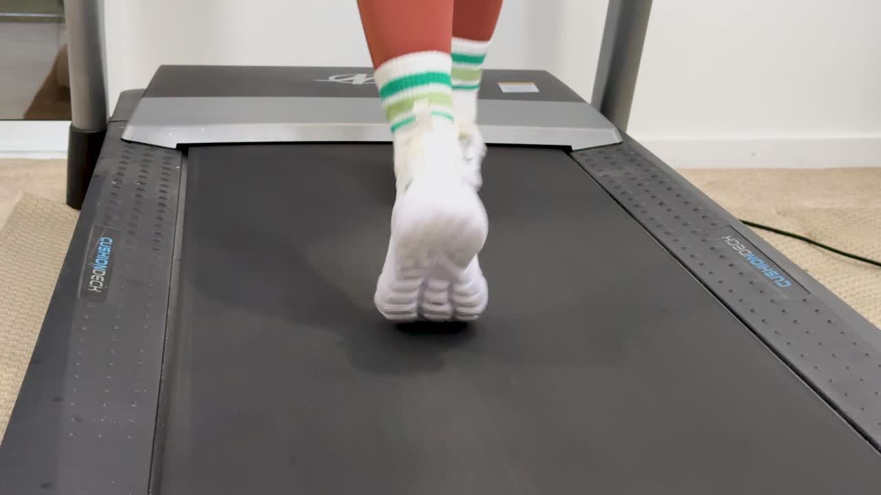 A woman runs on a treadmill in a well-lit home gym, focusing on fitness and health