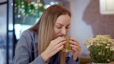 uma jovem loira bonita a comer um hambúrguer num restaurante de fast food.