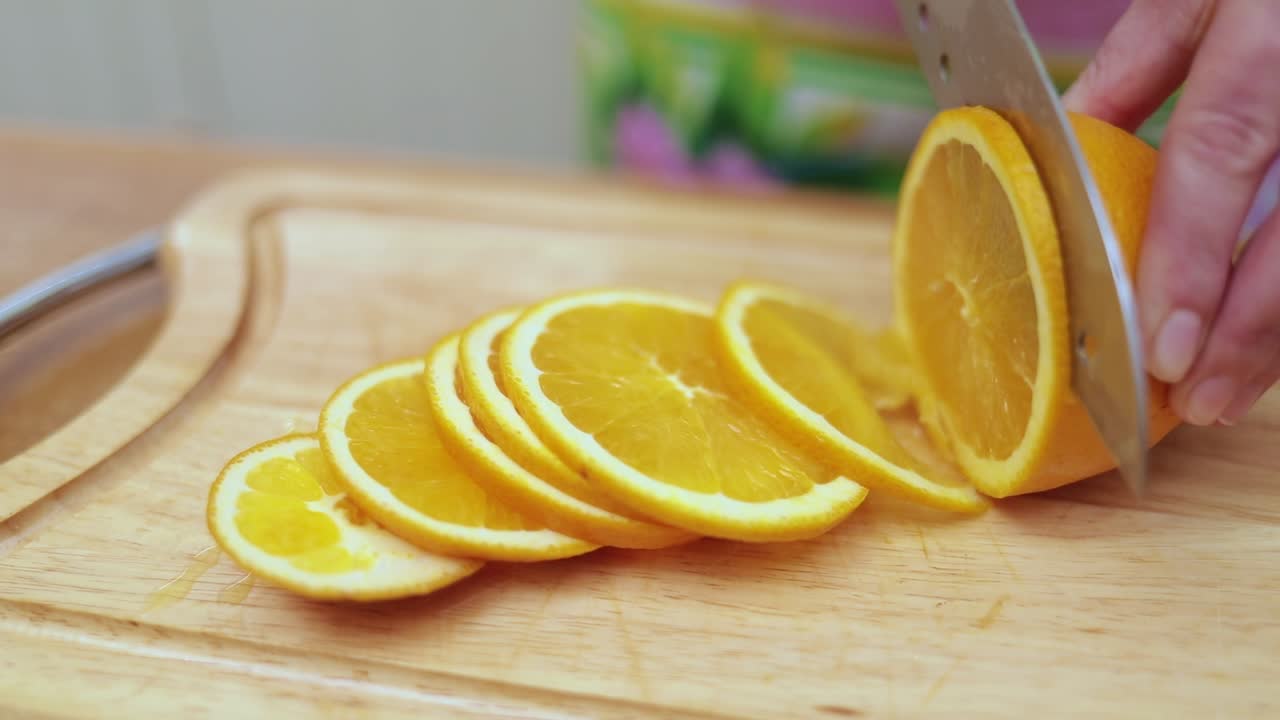 Women's hands Housewives cut with a knife fresh orange on the cutting Board of the kitchen table