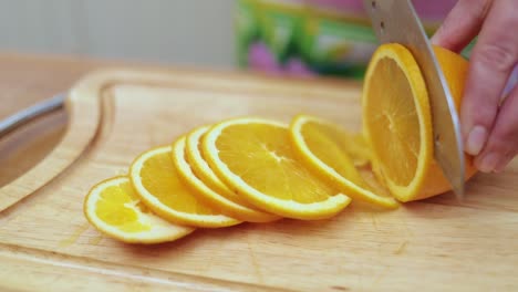 women's hands housewives cut with a knife fresh orange on the cutting board of the kitchen table